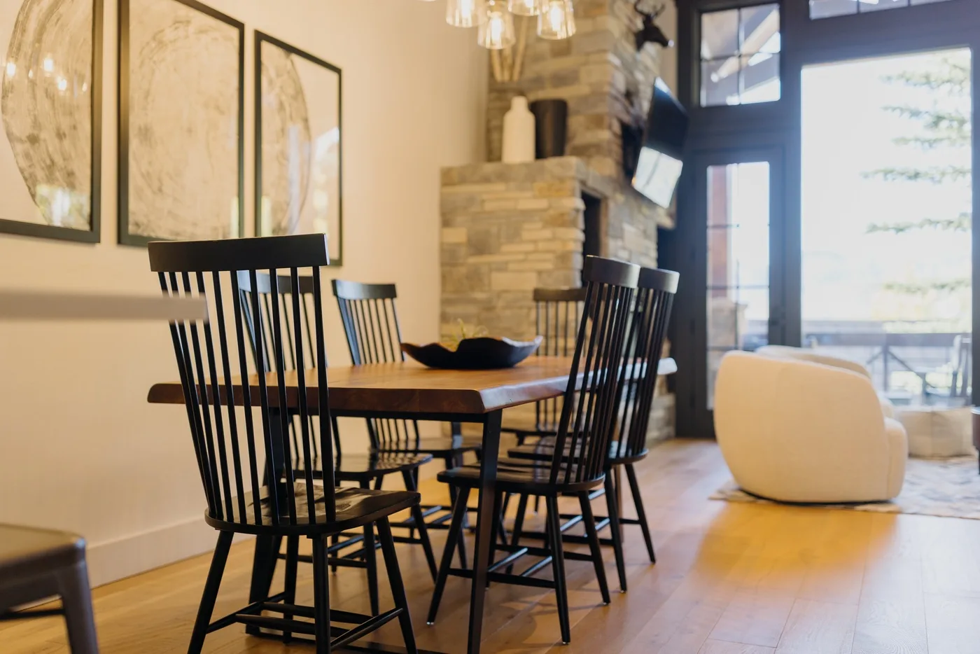 A dining area with a wooden table and dark chairs beside a stone fireplace.