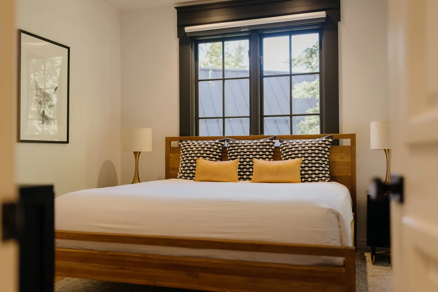 A bedroom with a wooden bed, patterned pillows, and a large window.
