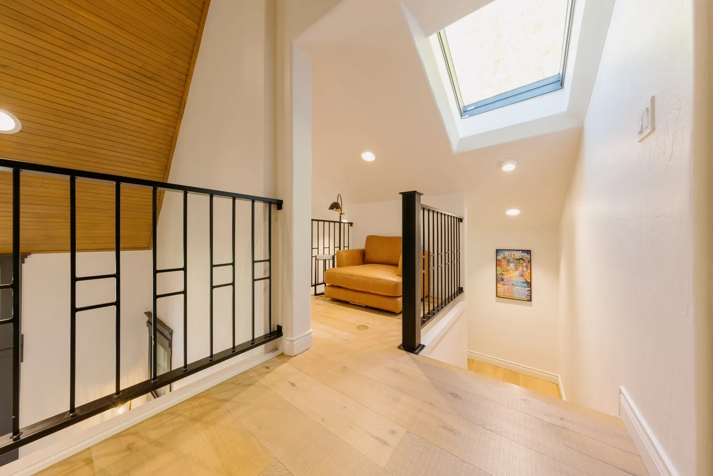 A bright upstairs landing with a skylight, black railings, and seating.