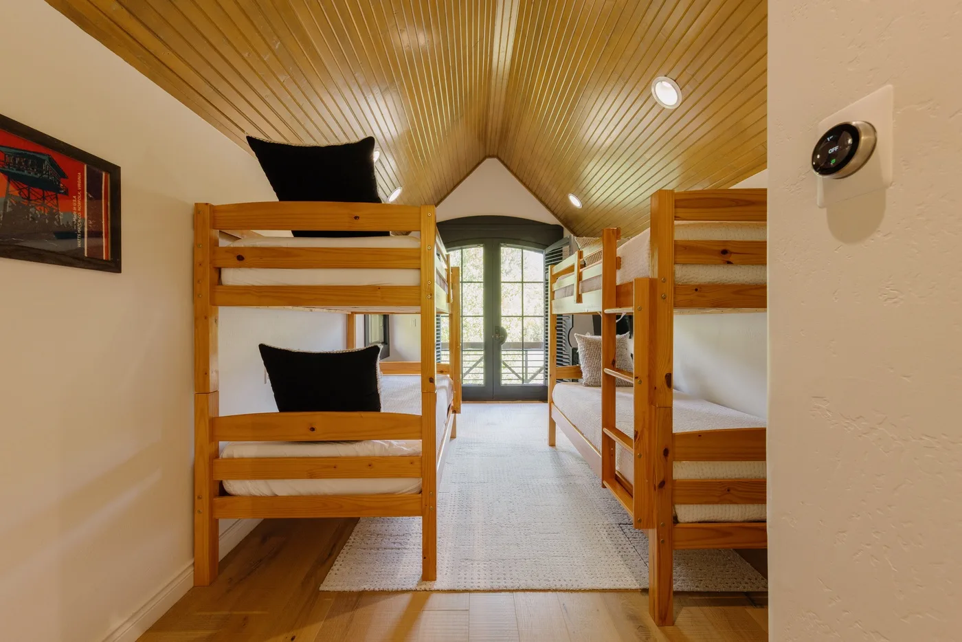 A bunk-bed room with a central walkway leading to glass doors.