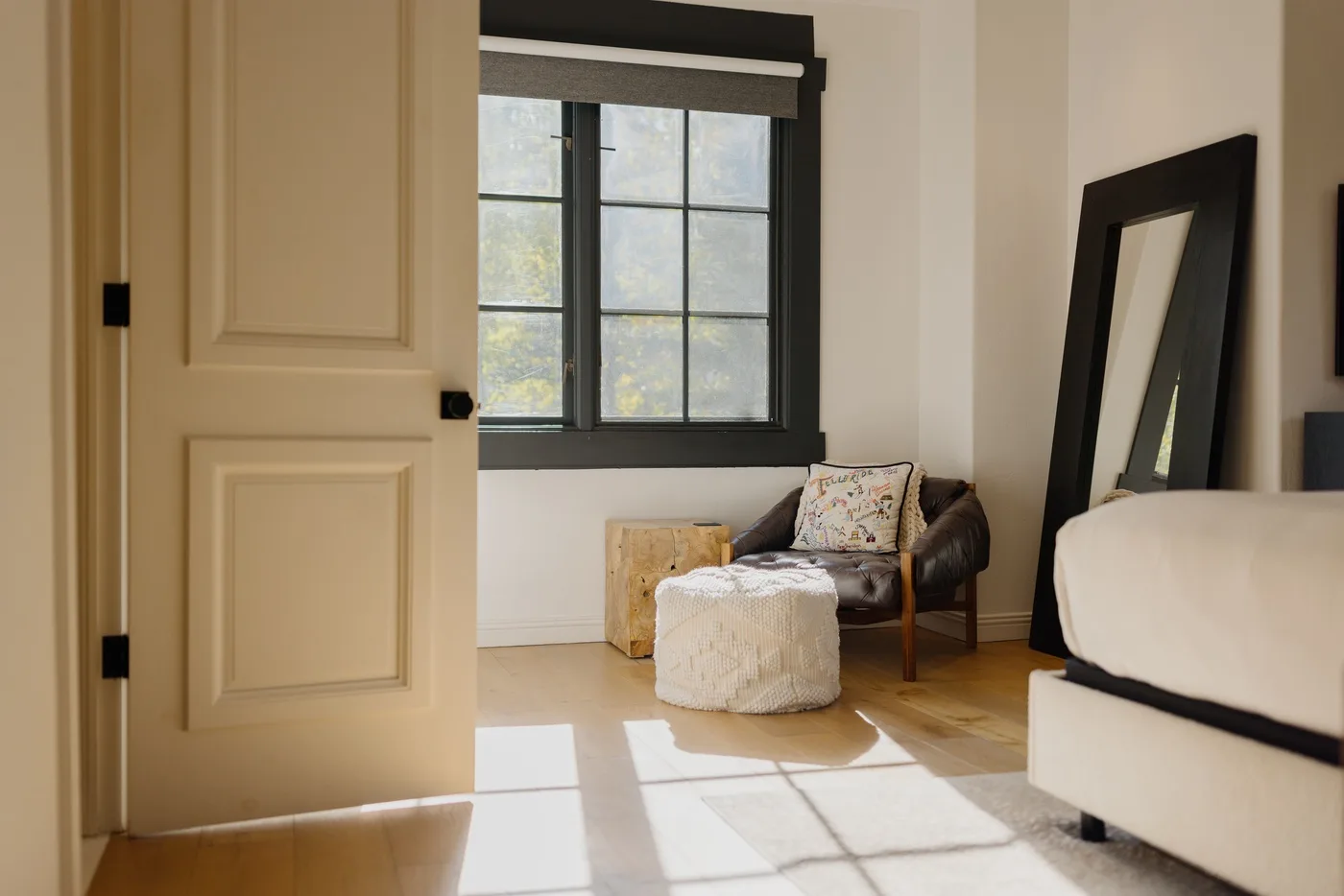 A bright bedroom with a window, a seating area, and a bed.