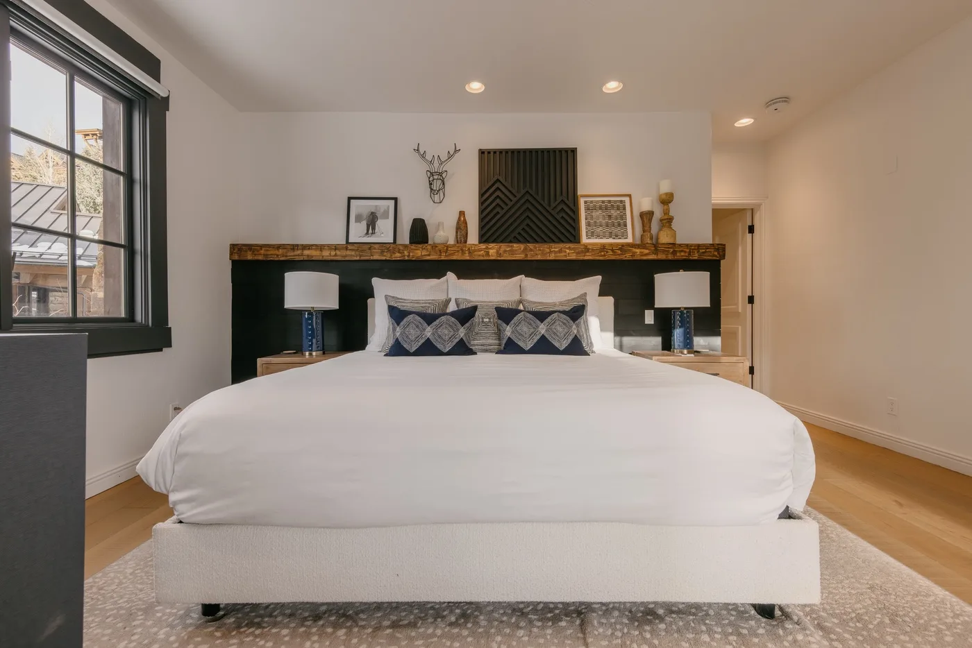 A bedroom with a neatly made bed, decorative pillows, and windowside seating.