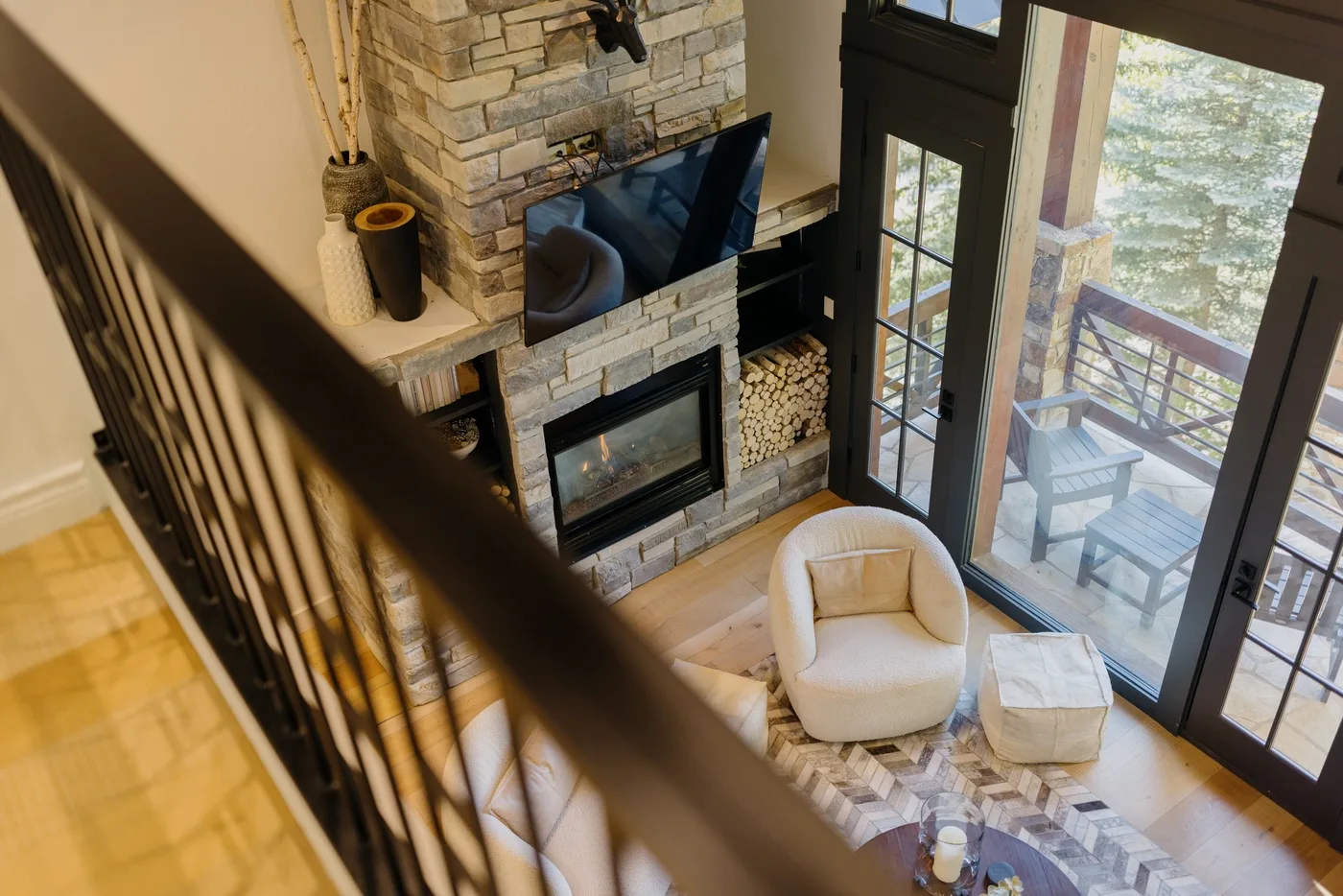 A living room with a stone fireplace, seating, and glass doors opening onto a deck.