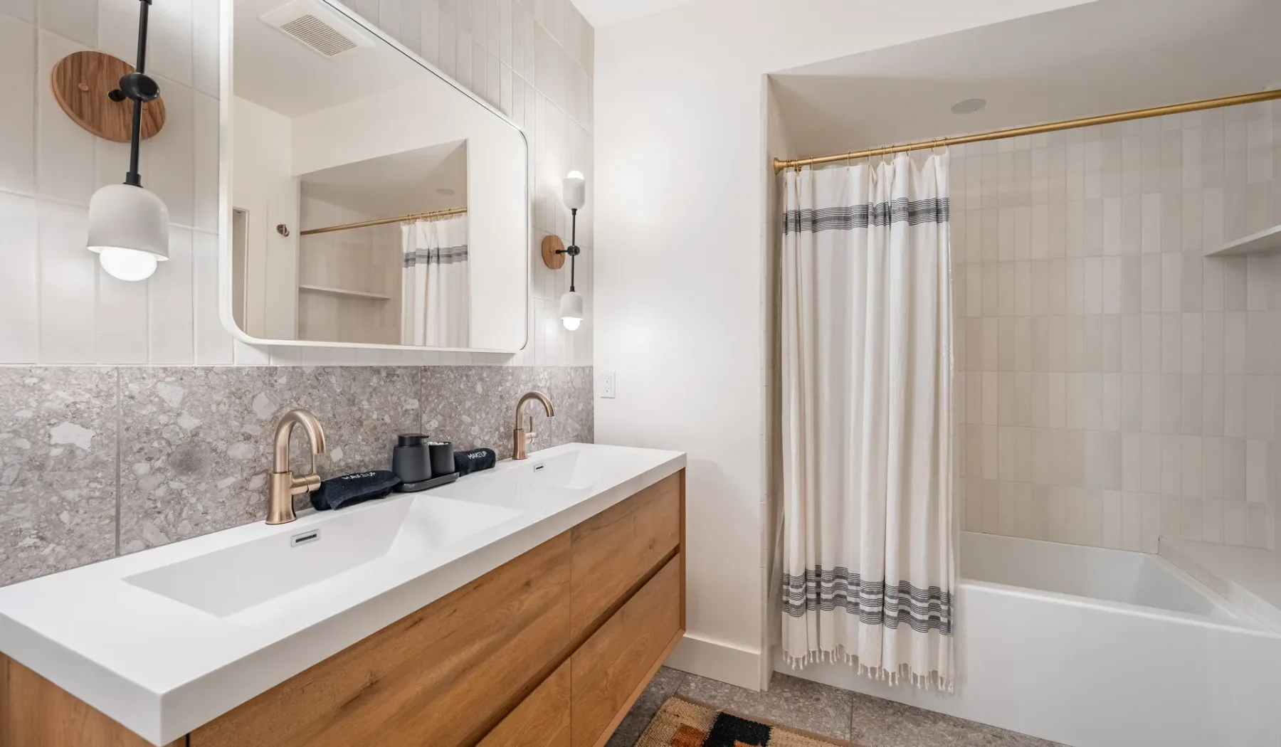 Un baño con un tocador largo, espejo y bañera con cortina.