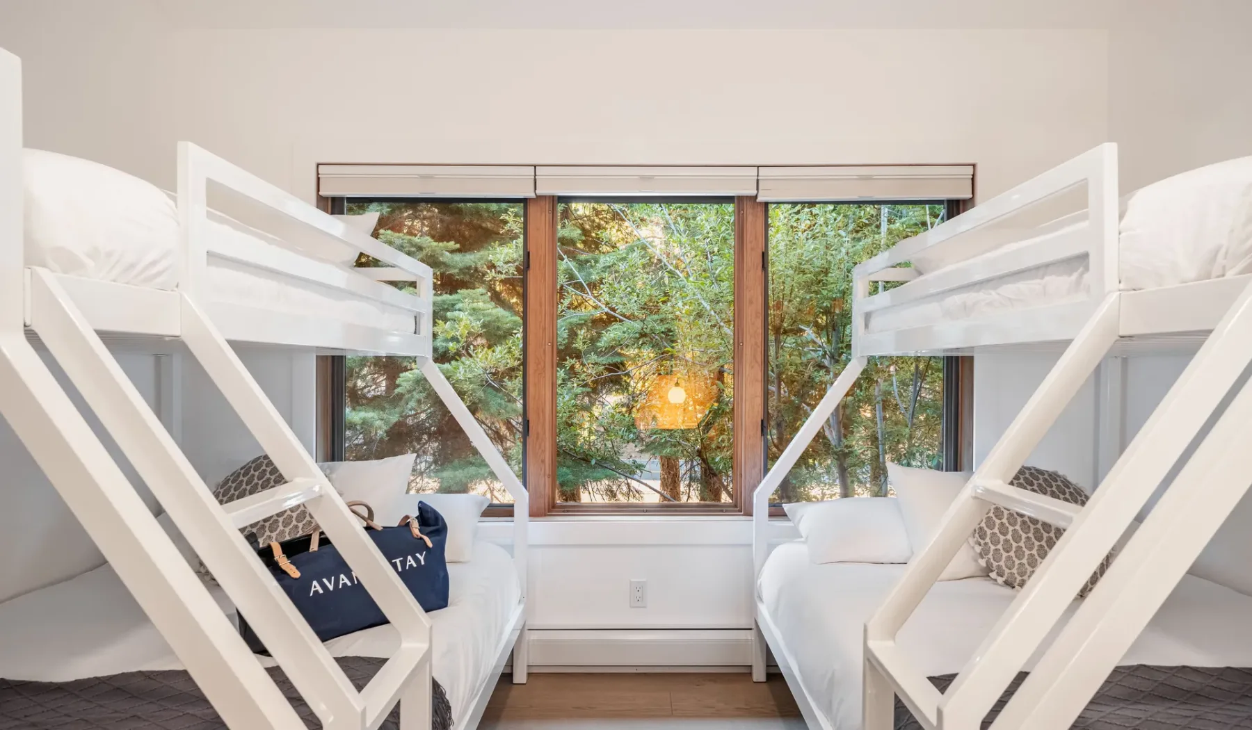 Un dormitorio luminoso con dos camas elevadas junto a una ventana grande con vistas a la vegetación.
