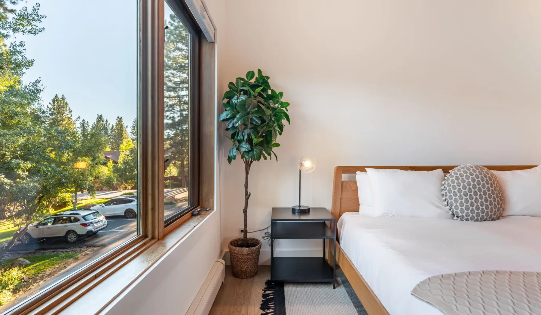 Un dormitorio luminoso con una cama junto a una gran ventana con vista a los árboles.