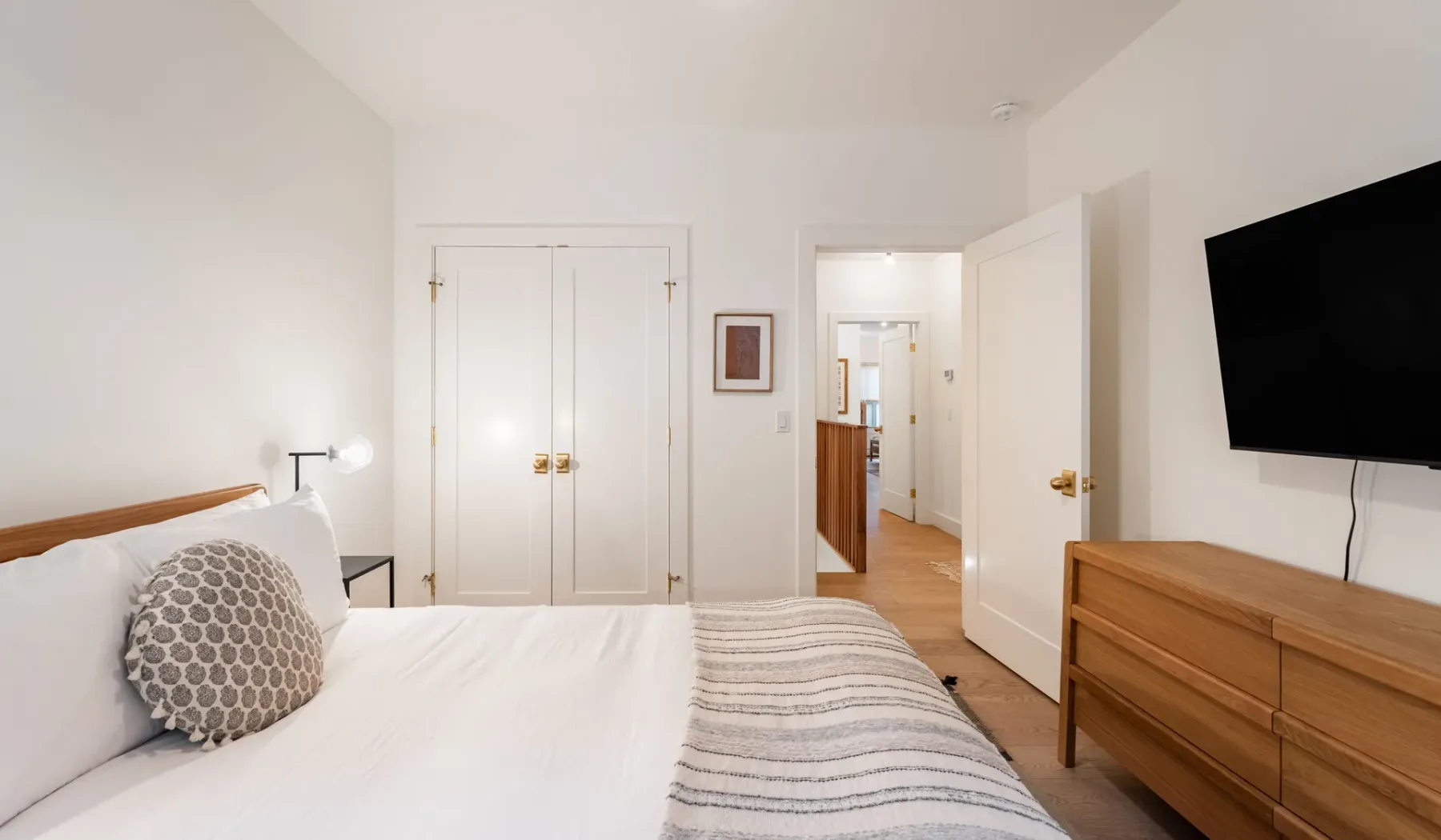 Dormitorio con una cama, una cómoda de madera y un televisor en la pared.