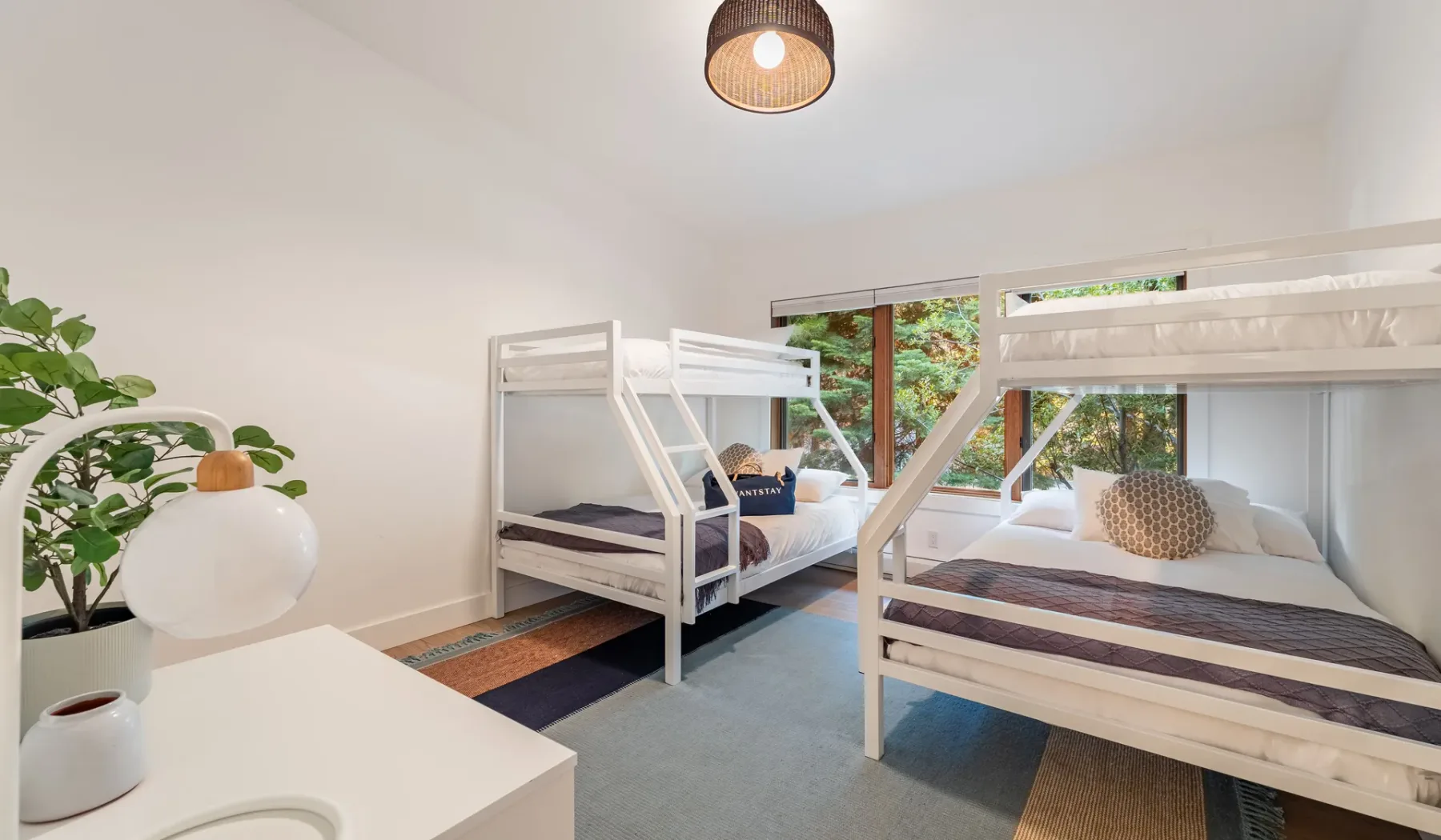 Un dormitorio luminoso tiene dos literas junto a grandes ventanas y una planta frondosa.