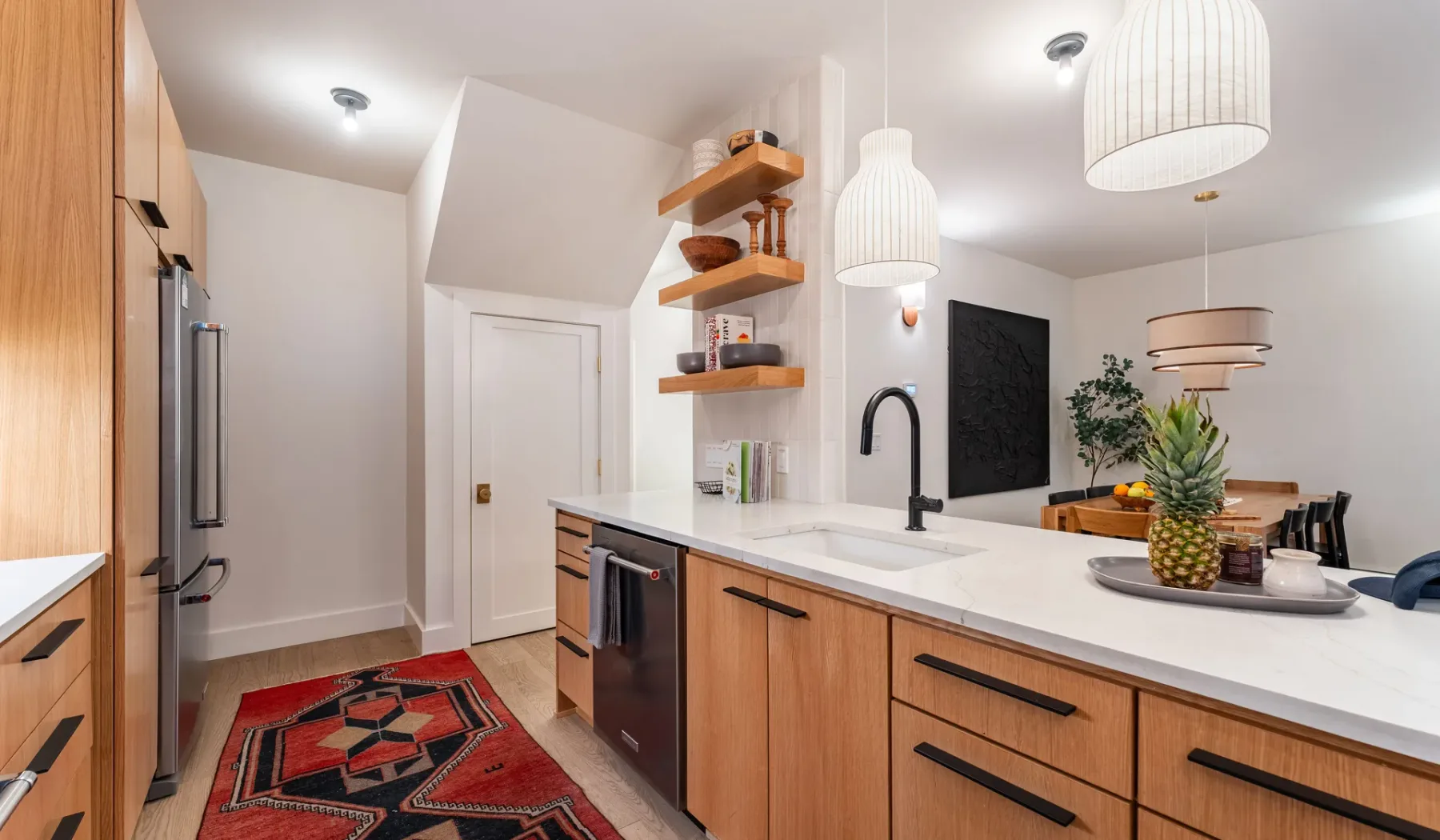 Una cocina luminosa con una isla blanca, gabinetes de madera y luces colgantes.