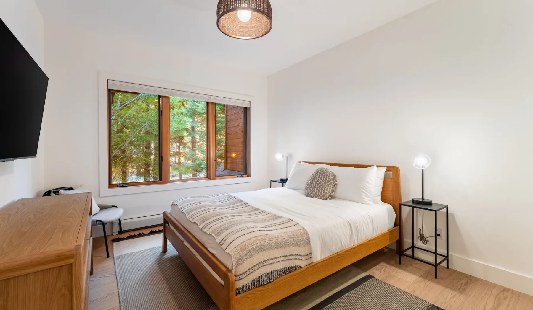 Un dormitorio con una cama de madera, mesitas de noche y una ventana grande.