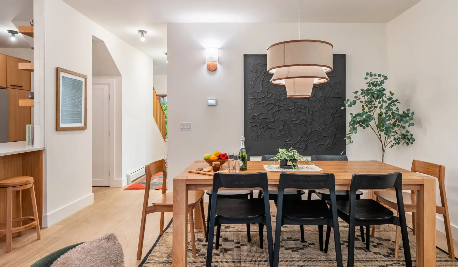 Comedor con una mesa de madera, sillas negras y una planta frondosa.