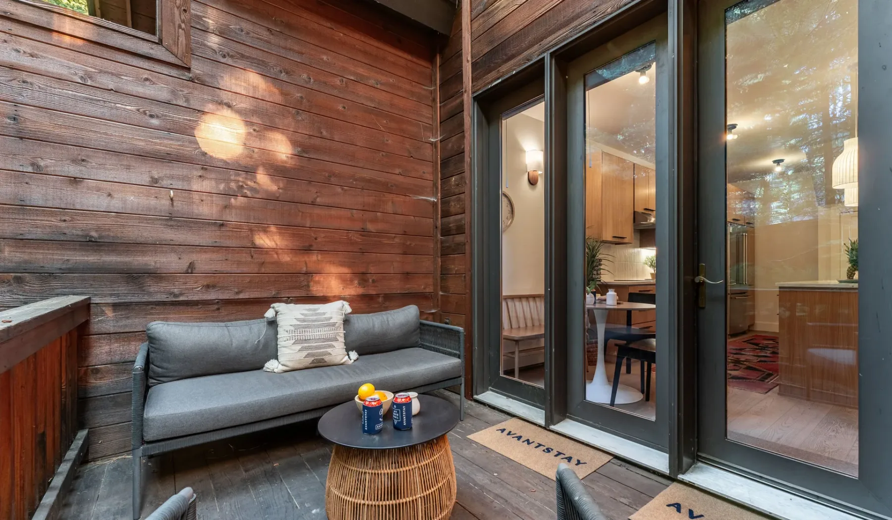 Un patio revestido de madera con asientos y puertas de vidrio que dan al interior.