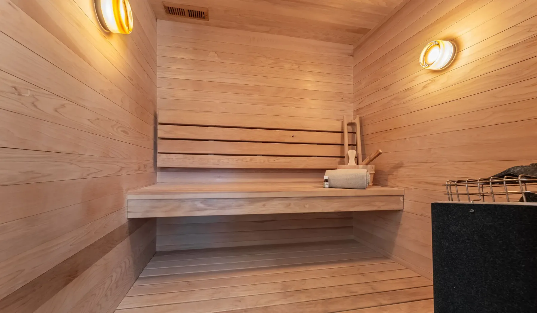 Una sauna revestida de madera con un banco elevado y un cubo.