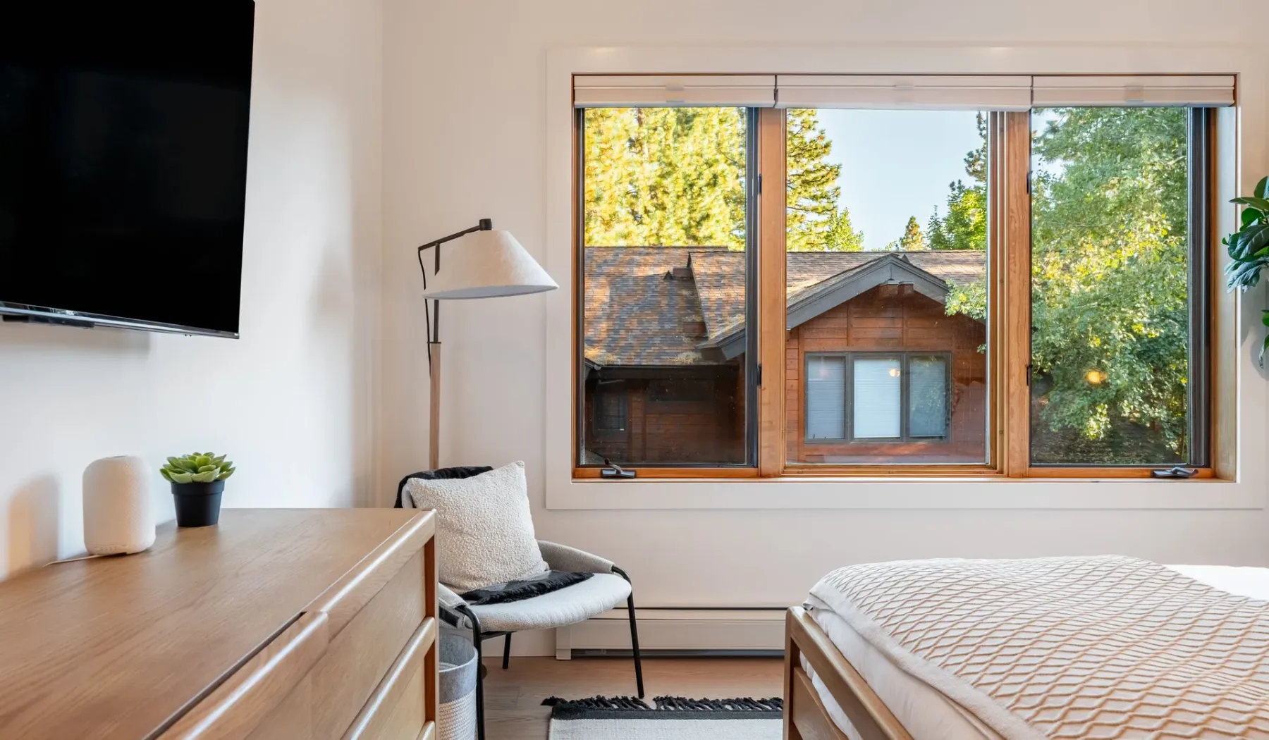 Un dormitorio luminoso con una cama, asientos y una ventana grande con vistas a los árboles.