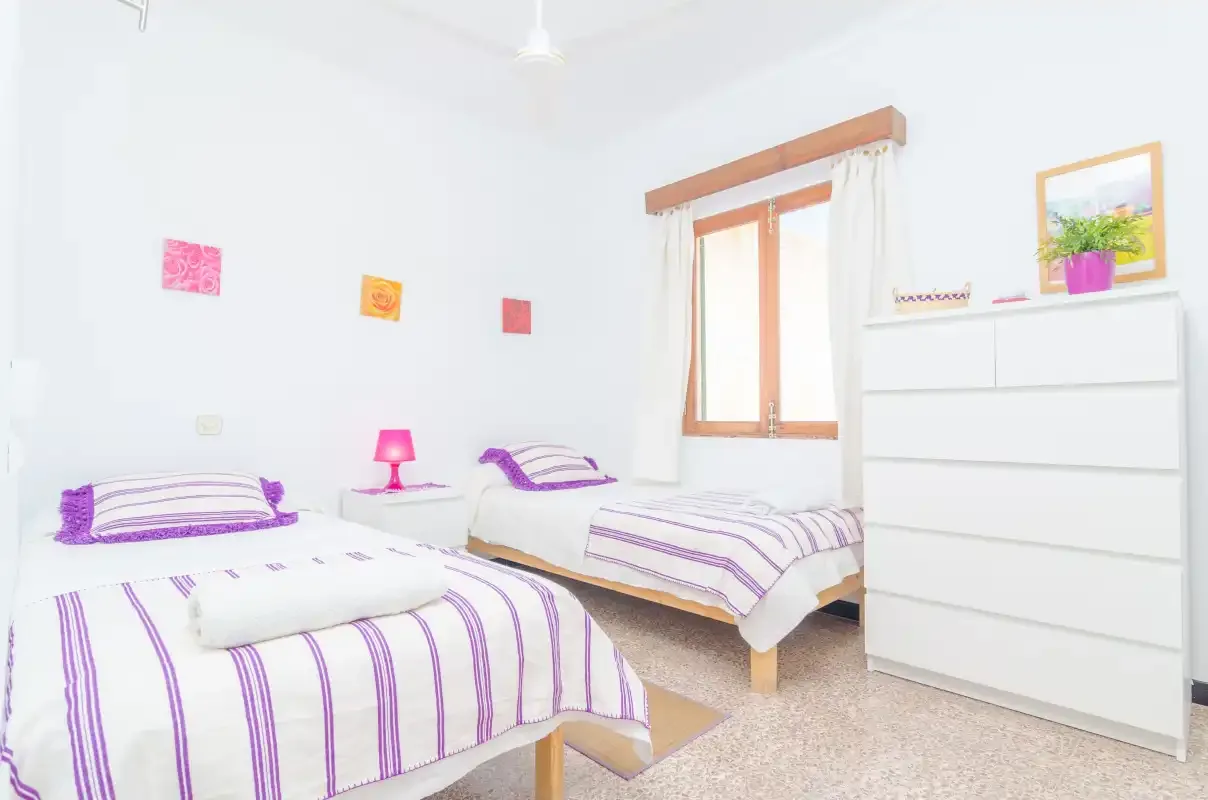 Un dormitorio luminoso con dos camas vestidas con ropa de cama blanca y morada.