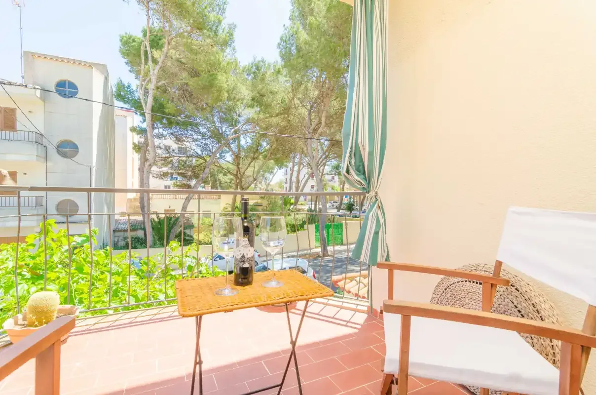 Un balcón soleado con una mesa pequeña, asientos y vistas a los árboles.