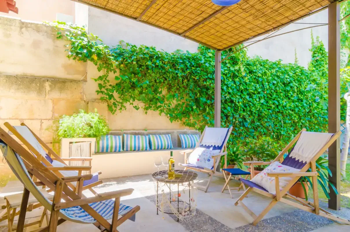 Un patio exterior sombreado con asientos y vegetación trepadora.