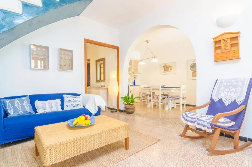 Una luminosa sala de estar se abre a un comedor, con asientos azules y una mesa de centro tejida.