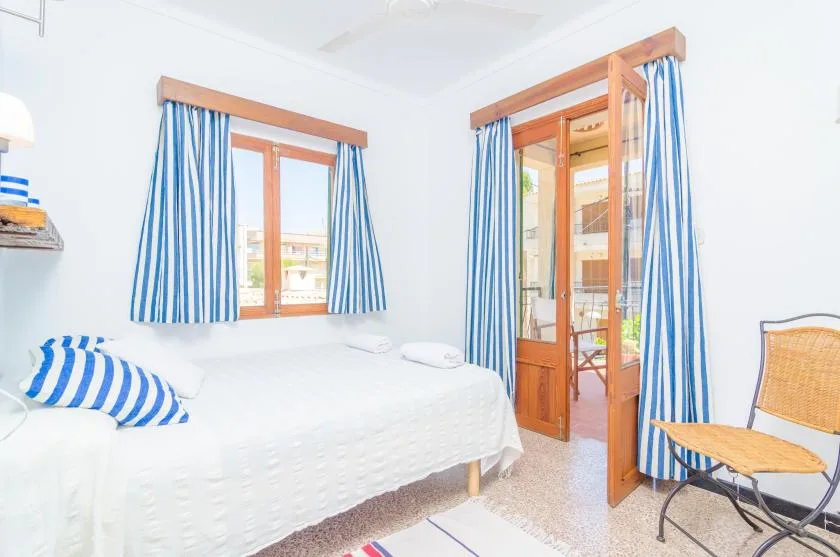 Un dormitorio luminoso con una cama, cortinas a rayas y una silla de madera.