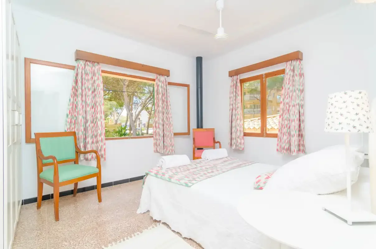 Un dormitorio luminoso con una cama, cortinas estampadas y una silla verde.
