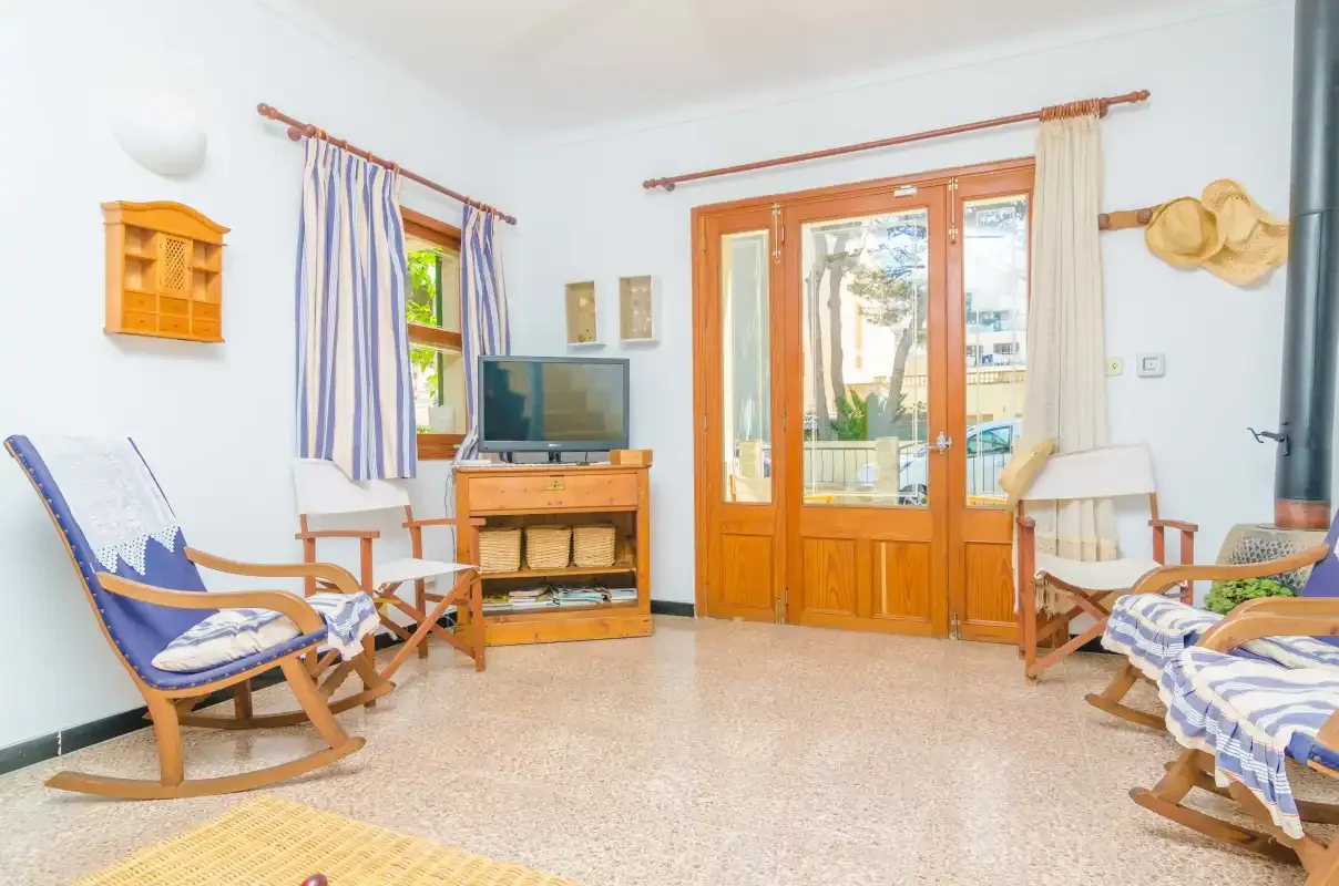 Sala de estar luminosa con mecedoras de madera y puertas acristaladas que dan a un balcón.