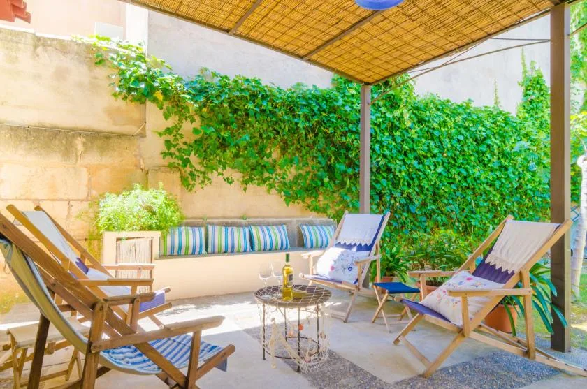 Un patio al aire libre con asientos de descanso bajo un toldo tejido y vegetación frondosa.