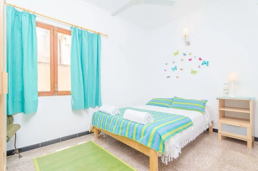 Un dormitorio luminoso con una colcha a rayas y cortinas turquesas.