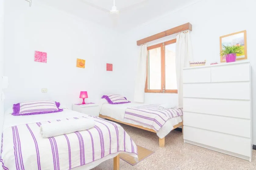 Un dormitorio luminoso con dos camas vestidas con ropa de cama blanca y morada.