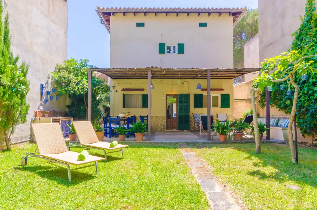 Una casa de dos plantas da a un jardín soleado con asientos al aire libre.