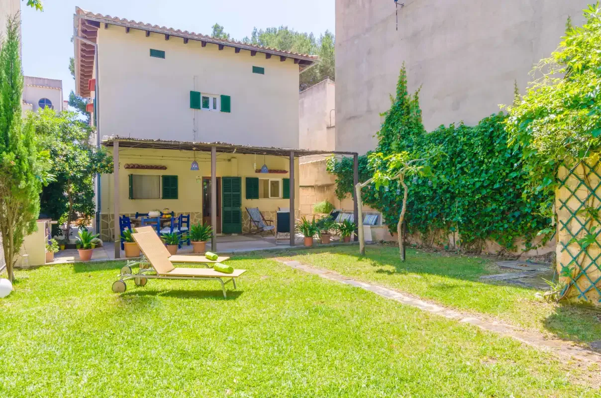 Un patio ajardinado con césped, tumbonas y una casa de dos plantas.