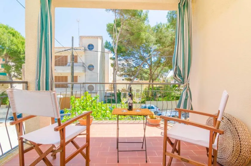 Una zona de estar en un balcón con una mesa pequeña da a árboles y edificios cercanos.