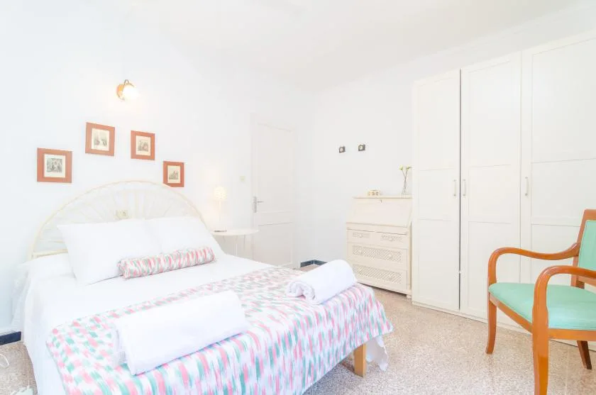 Un dormitorio luminoso con una cama, armarios blancos y una silla verde.
