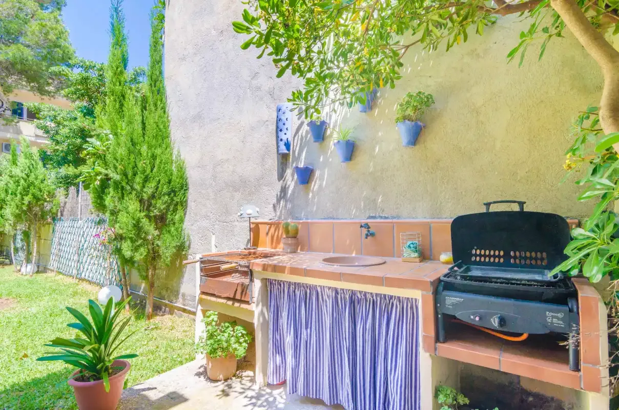 Un patio exterior con una encimera de azulejos, una parrilla y plantas en macetas.