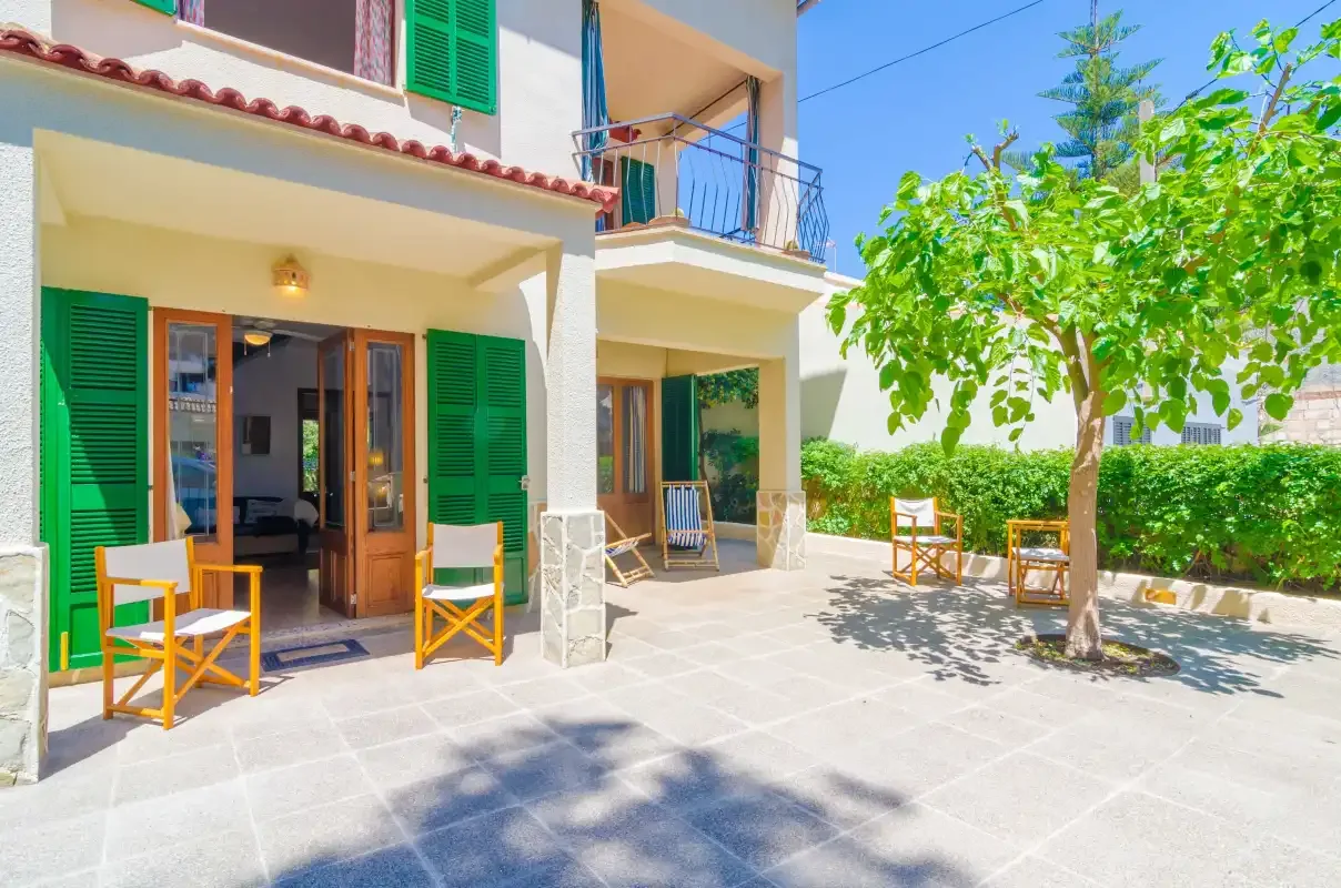 Un patio soleado con asientos al aire libre y puertas con contraventanas verdes.