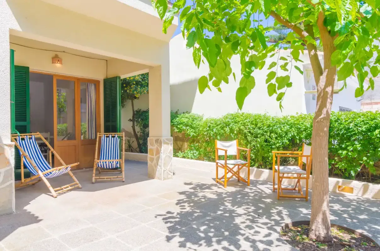 Un patio sombreado con asientos al aire libre junto a puertas de vidrio y árboles frondosos.