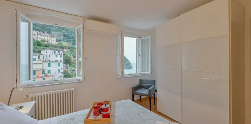 Una habitación luminosa con ventanas abiertas, un radiador y una mesa pequeña.