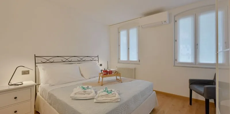 Un dormitorio con una cama bien tendida y ventanas a lo largo de la pared.