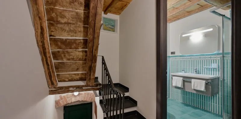 Una escalera interior junto a un baño con azulejos turquesa.