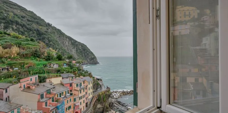 Un pueblo costero y una ladera verde empinada se ven a través de una ventana abierta.