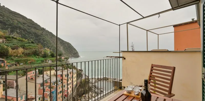 Un balcón da a edificios costeros y al mar, con una colina a lo lejos.