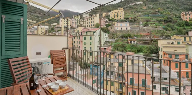 Una zona de estar en un balcón da a edificios en la ladera y vegetación en terrazas.