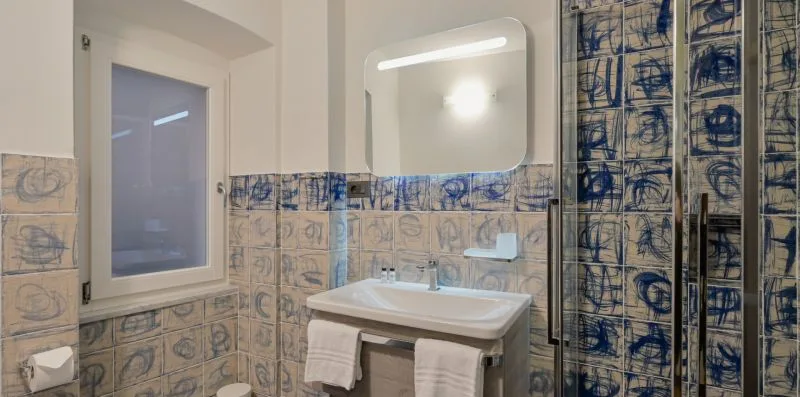 Un baño alicatado con lavabo, espejo iluminado y ducha.