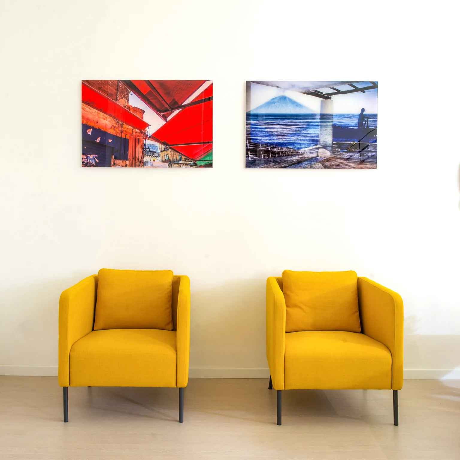 A bright sitting area with two yellow armchairs beneath framed artwork.