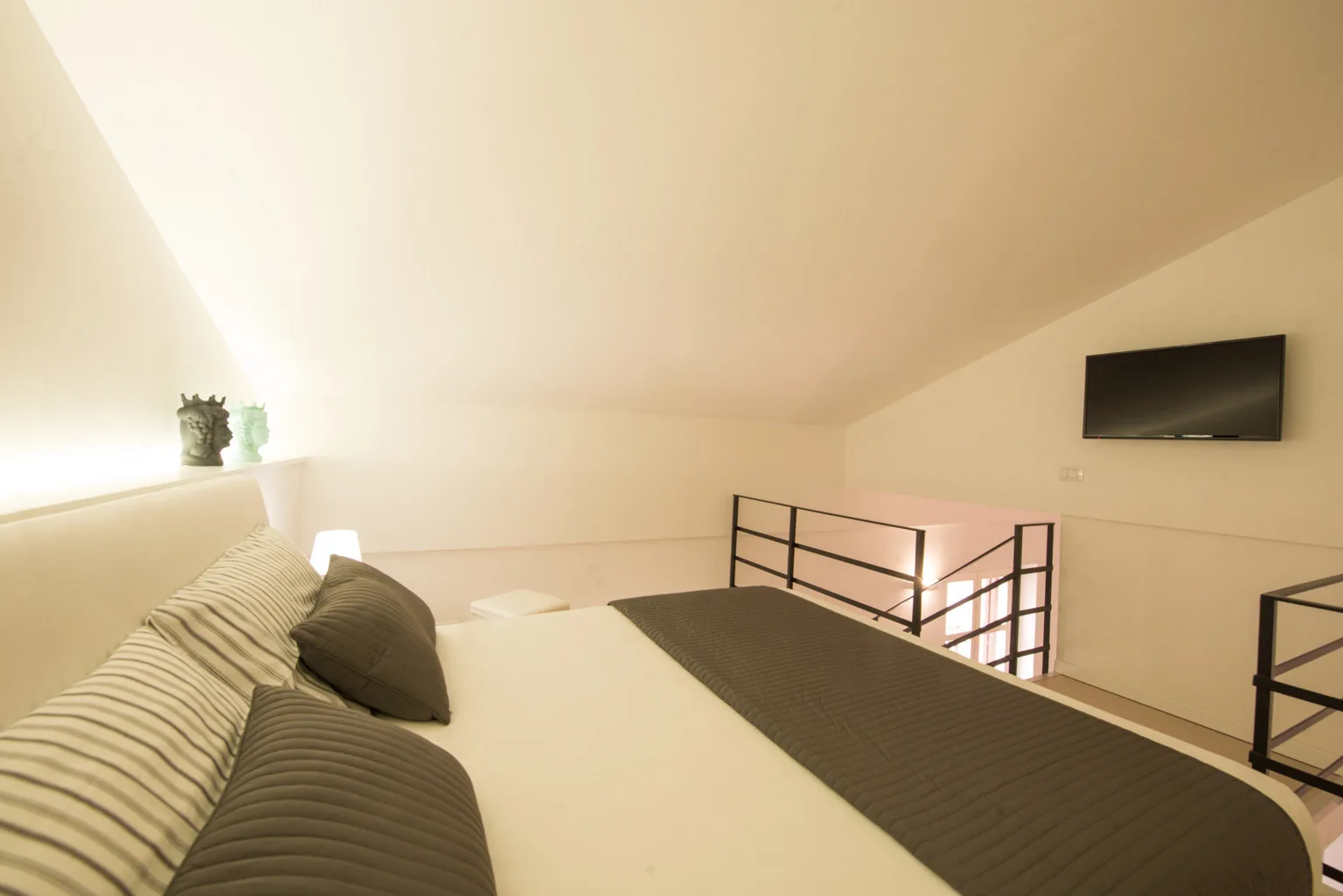 A loft bedroom with a bed, dark pillows, and a wall-mounted television.