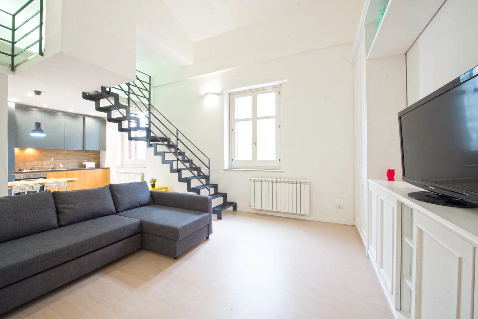 A bright living room with a sectional sofa, staircase, and television.