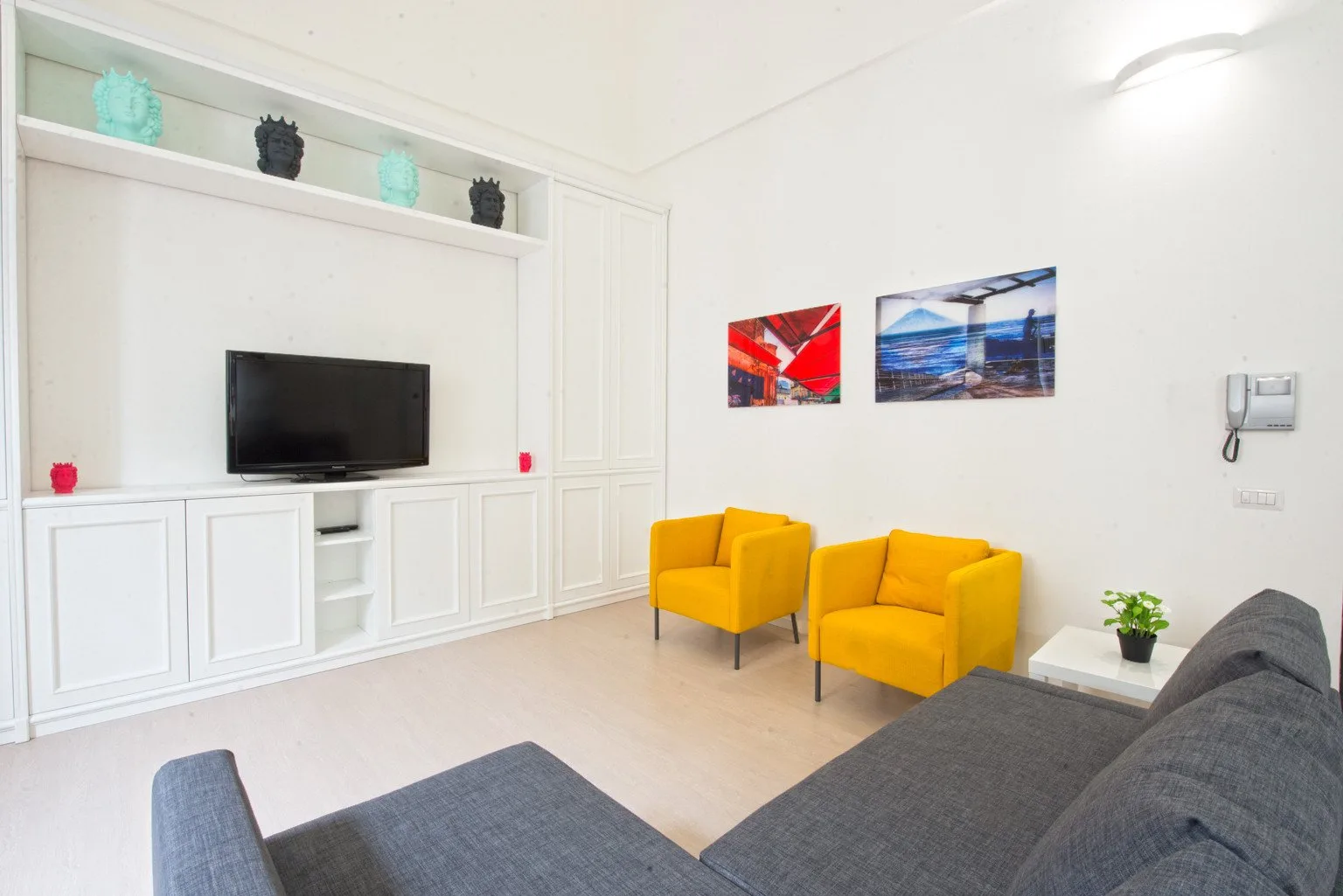 A living room with yellow seating, a television, and colorful wall art.