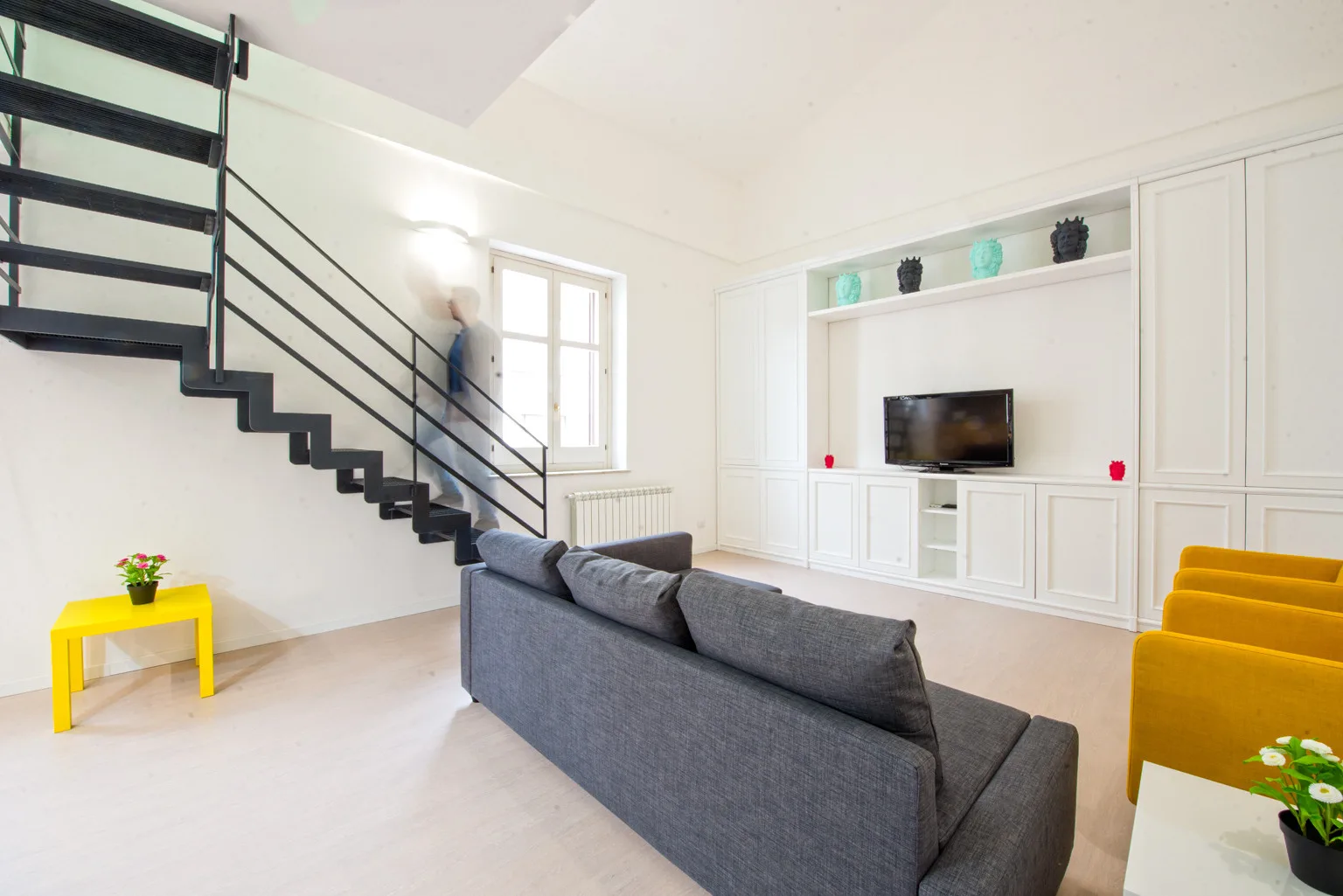 A bright living room with a gray seating area, television, and staircase.