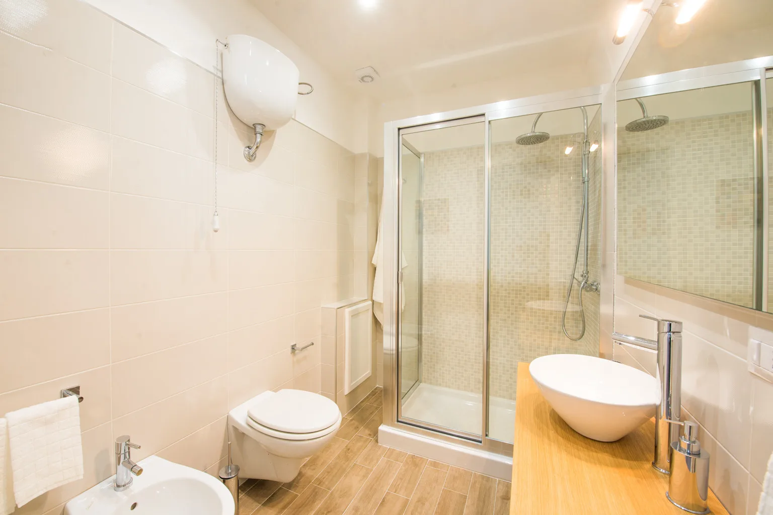 A bright tiled bathroom with a glass shower, sink, and toilet.