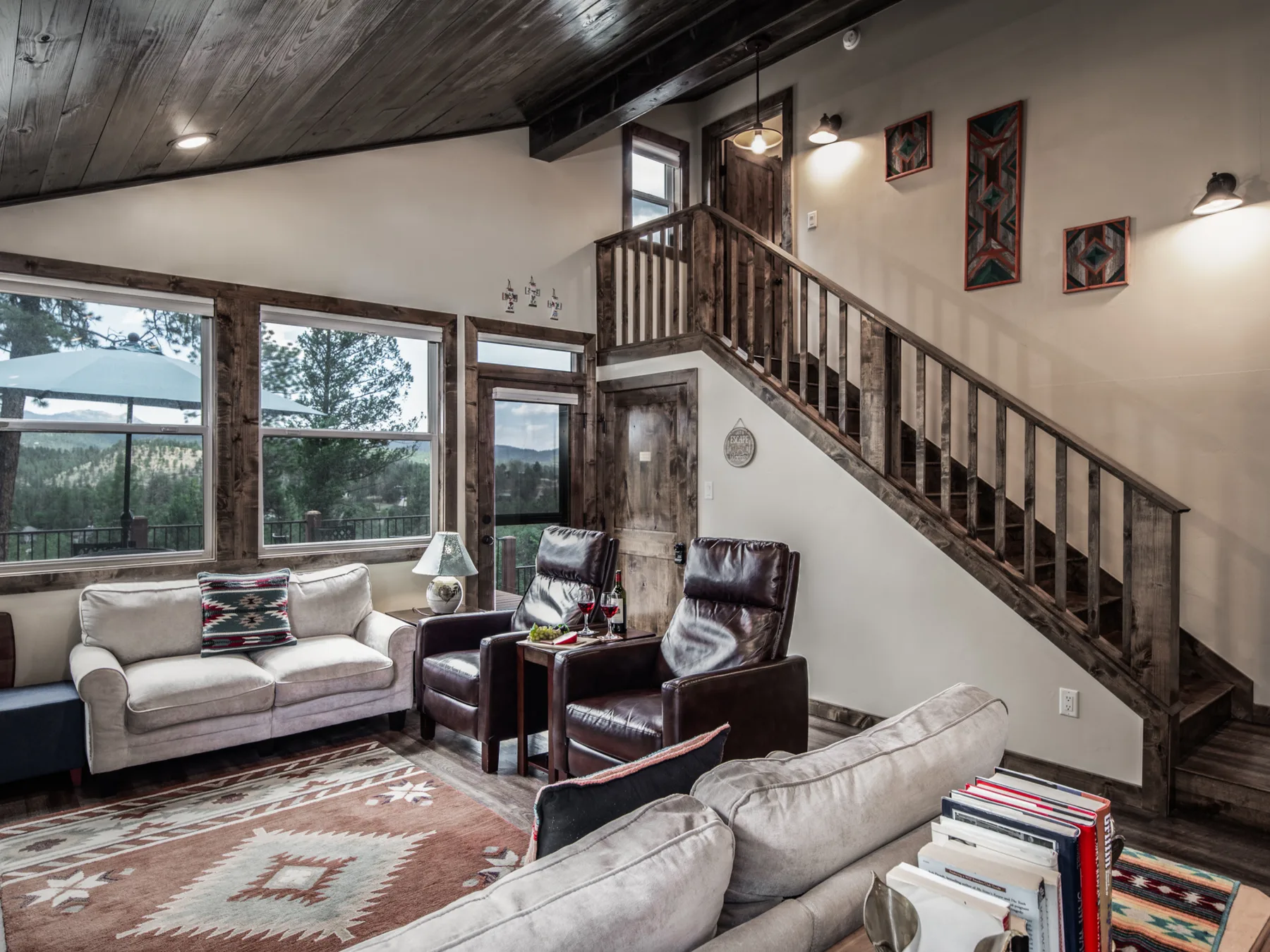 A living room with seating arranged beside large windows and a wooden staircase.
