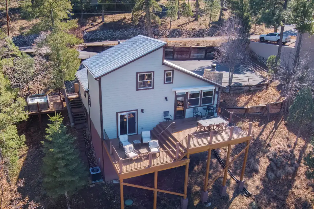 A raised house with a wooden deck sits among trees on a wooded slope.